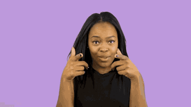 a woman in a black shirt is pointing at her hair on a purple background