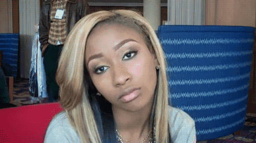 a woman with blonde hair looks at the camera with a man in the background