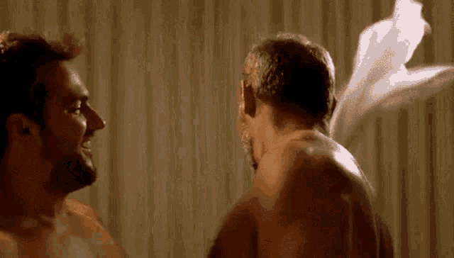 two shirtless men are standing next to each other and one of them has wings .