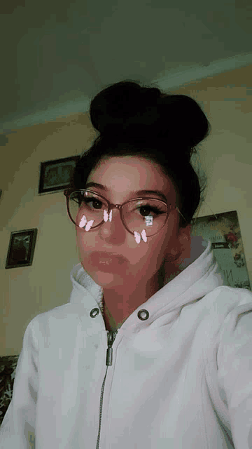 a woman wearing glasses and a pink hoodie has a bun on her head