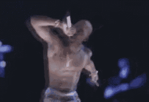 a man without a shirt is singing into a microphone on stage .