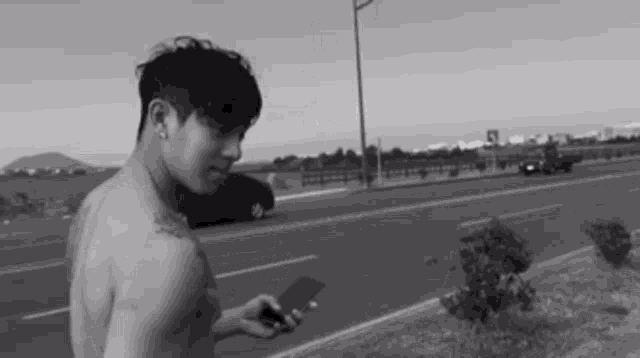 a shirtless man is standing on the side of a road looking at his phone .