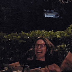 a woman wearing glasses is laughing while sitting at a table with a man