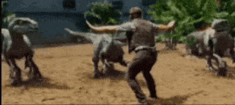 a man is running away from a herd of dinosaurs in a dirt field .