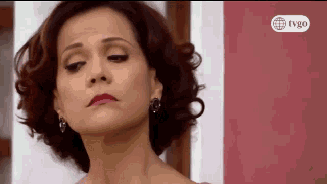 a woman 's face is shown in front of a pink wall with tvgo written on it