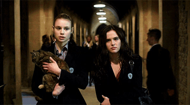 two women are walking down a hallway one holding a cat