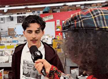 a man in a plaid hat is talking into a microphone in a store