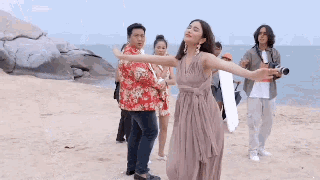 a group of people are standing on a beach with their arms outstretched and a woman in a dress .