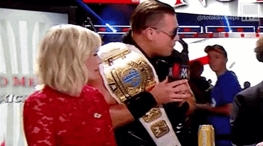a man and a woman are standing next to each other in a ring holding a championship belt .