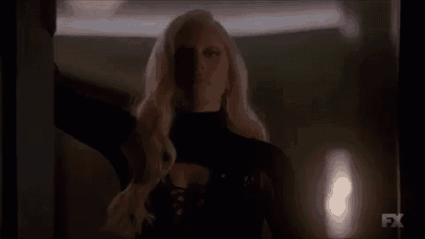 a blonde woman in a black dress is standing in a dark room .