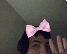 a man with a pink bow on his head is giving a peace sign