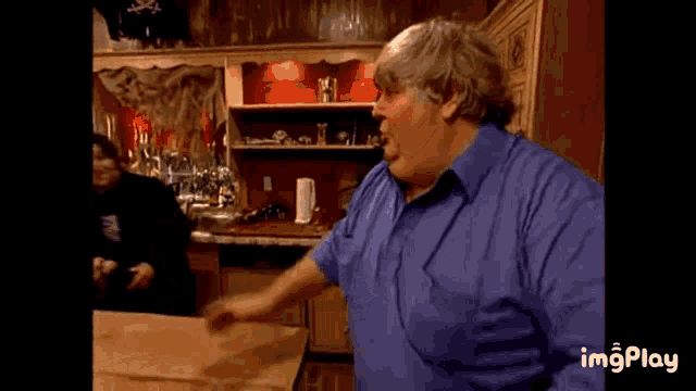 a man in a blue shirt is standing in front of a counter in a kitchen .