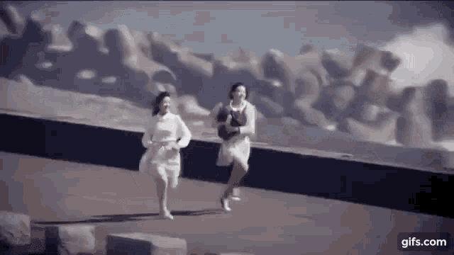 two women in white dresses are running across a bridge .