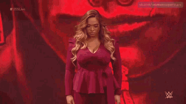 a woman in a red dress is standing in front of a red background with a w logo on it .