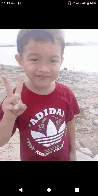 a young boy wearing an adidas t-shirt giving a peace sign
