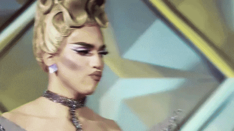 a drag queen wearing a choker and earrings is standing in front of a colorful background .