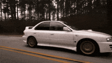 a white car is driving down a road with a forest in the background