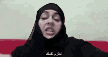 a woman in a hijab is sitting on a red couch and talking .