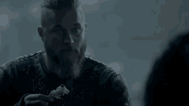 a man with a beard is holding a piece of food in his hand .