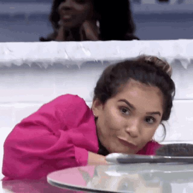 a woman in a pink jacket is sitting at a table with her head on the table .