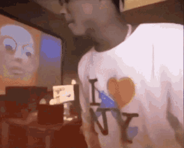 a man wearing a white t-shirt that says i love ny is standing in front of a screen .