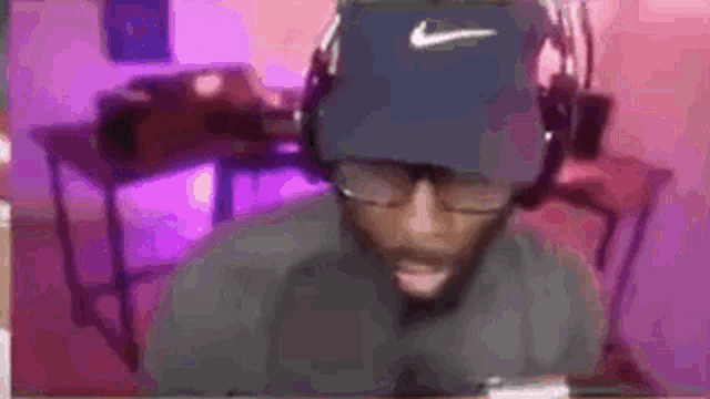 a man wearing a nike hat and headphones is sitting in front of a pink wall .