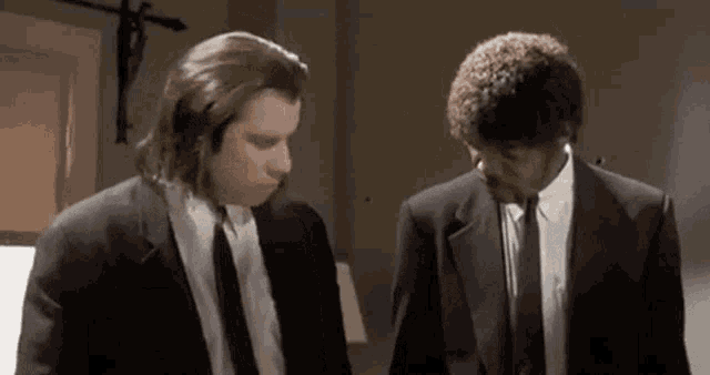 two men in suits and ties are standing next to each other in a room and talking .