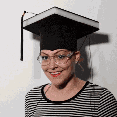 a woman wearing a graduation cap and glasses smiles for the camera