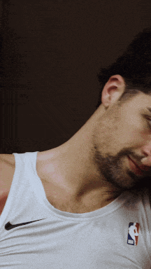 a man wearing a white nike tank top with a nba logo on his chest