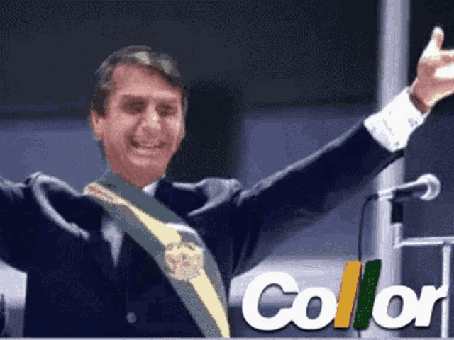 a man in a suit and tie is standing in front of a microphone with his arms in the air .
