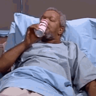 a man in a hospital bed is drinking a cup of water .