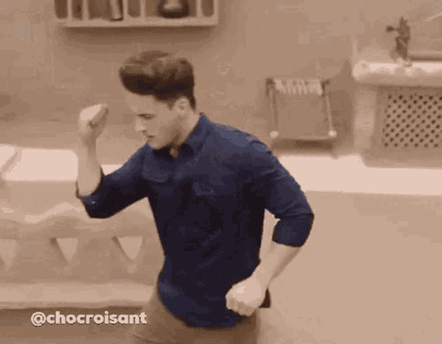 a man in a blue shirt is dancing in a bathroom with his hands in the air .