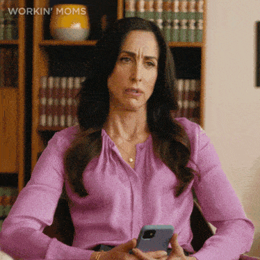 a woman in a purple shirt is holding a cell phone and the words workin ' moms are on the bottom