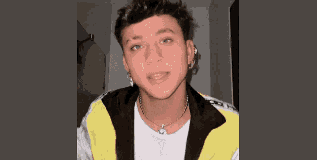 a young man wearing a white shirt and a yellow jacket is looking at the camera