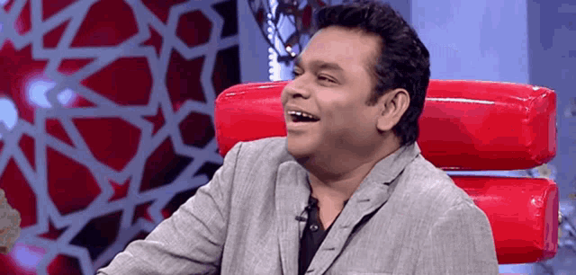 a man in a suit is sitting in a red chair and smiling