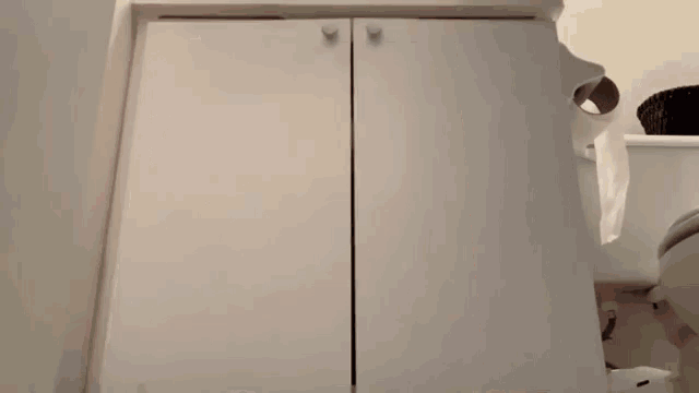 a person is peeking out from behind a white cabinet in a bathroom