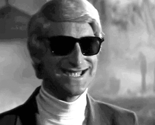 a man wearing sunglasses and a turtleneck is smiling in a black and white photo .