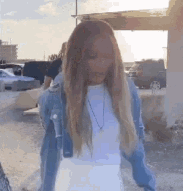 a woman is standing in a parking lot wearing a denim jacket and a white shirt .