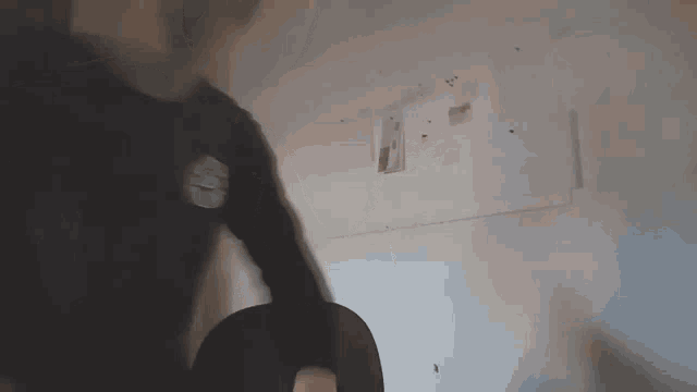 a man in a black shirt is standing in a room with a white wall .