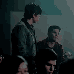 a man in a denim jacket is standing in front of a crowd of people in a dark room .