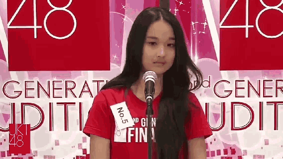 a girl is standing in front of a microphone wearing a red shirt with the number 5 on it