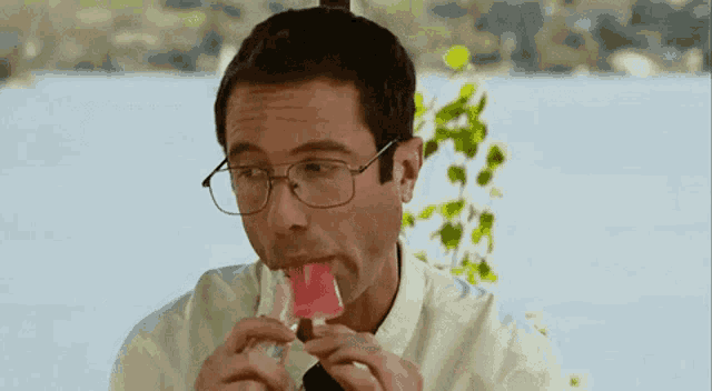 a man wearing glasses is eating an ice cream bar