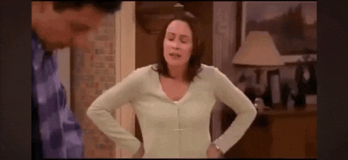 a woman is standing in a room with her hands on her hips and a man is standing behind her .