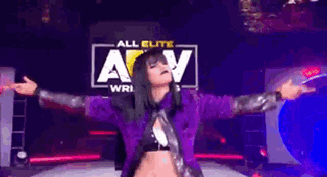 a woman in a purple jacket is standing on a stage with her arms outstretched .