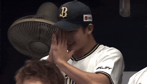 a baseball player covering his face with a hat with the letter b on it