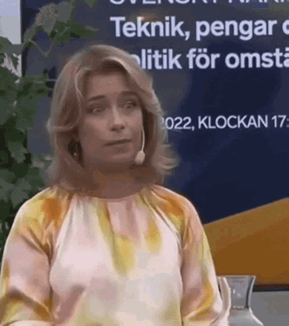 a woman wearing a tie dye shirt and a microphone is standing in front of a sign that says teknik