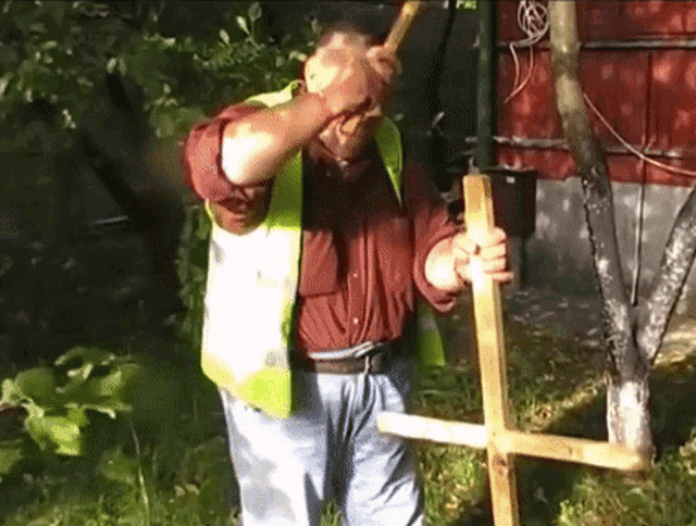 a man in a yellow vest holds a wooden cross