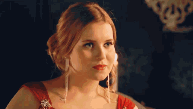 a woman in a red dress and earrings is looking at the camera