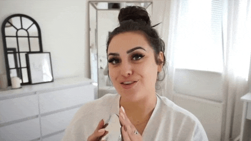 a woman is sitting in front of a mirror in a room holding a bottle of nail polish .