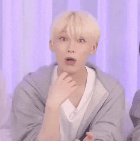 a young man with a surprised look on his face is wearing a gray hoodie and a white shirt .
